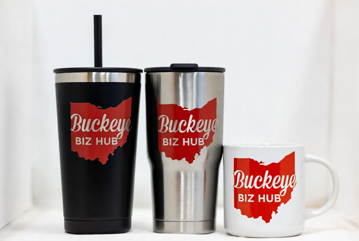 Black tumbler with a straw, a stainless tumbler and a white mug, each printed with the red Buckeye Biz Hub Ohio logo