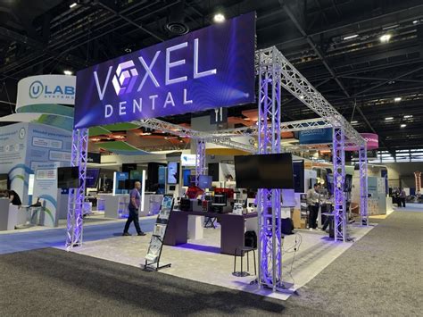 Large illuminated dental trade show booth with branded overhead truss signage and product displays