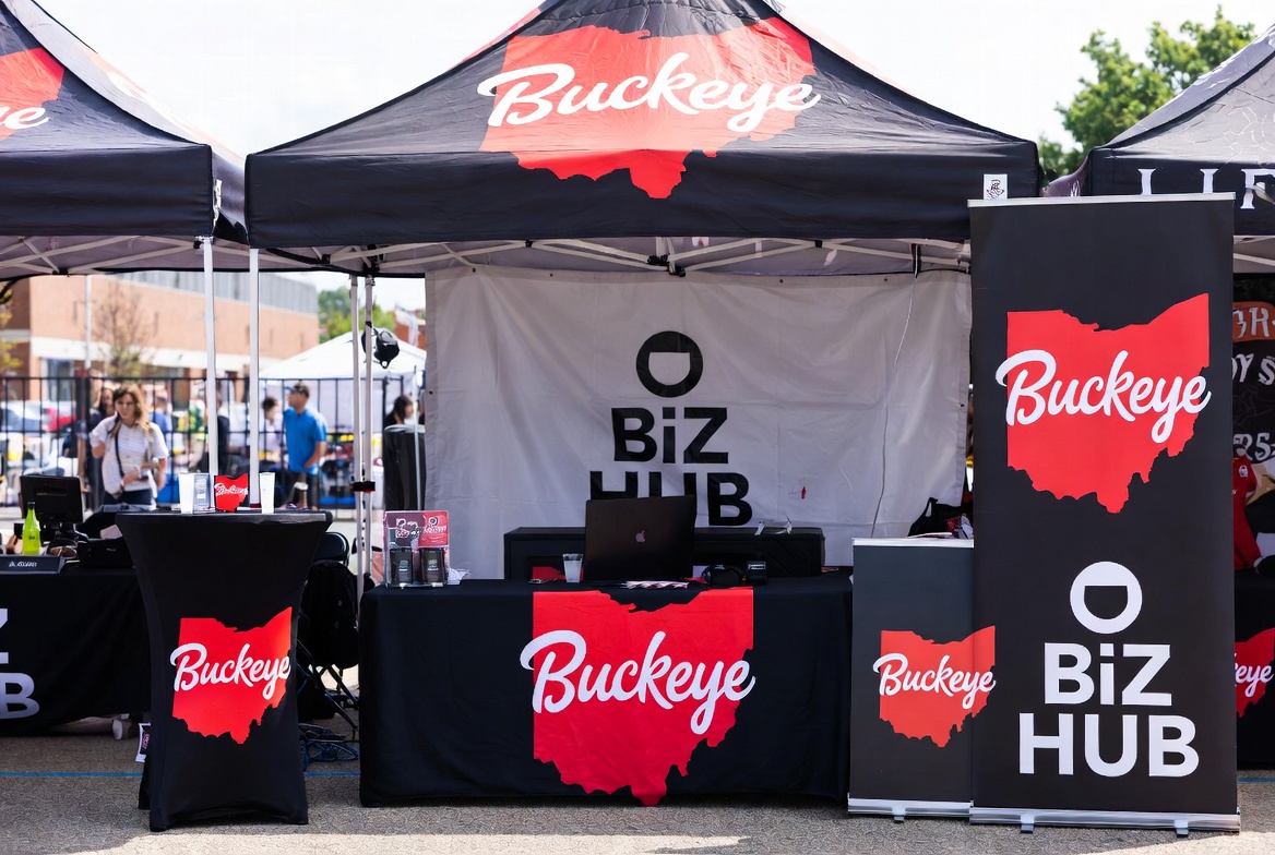 Outdoor event booth with black and red Buckeye Biz Hub pop-up tents, a printed table throw, a high-top table cover and retractable banners